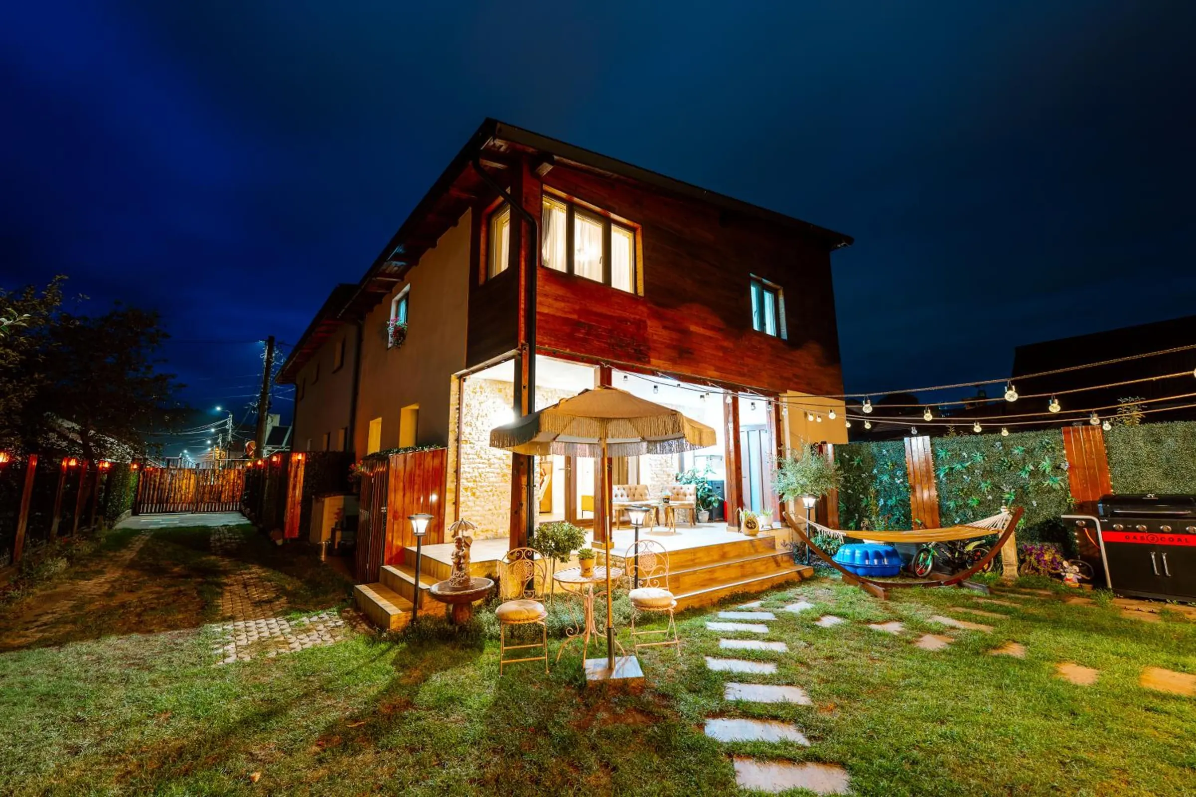 Casa Green Nest seara, cu terasa luminată, hamacul și grădina